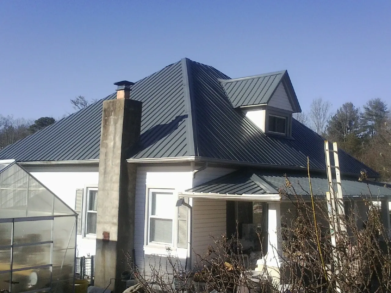 Dark blue standing seam metal roof on a white farmhouse with dormer — Slate & Tile Roof Repair by Roofing Brothers in Gilson