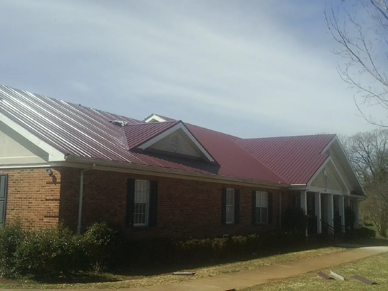 Red metal roof with gabled entries on a long brick building, from a Hail Damage Roof Repair job in Gilson