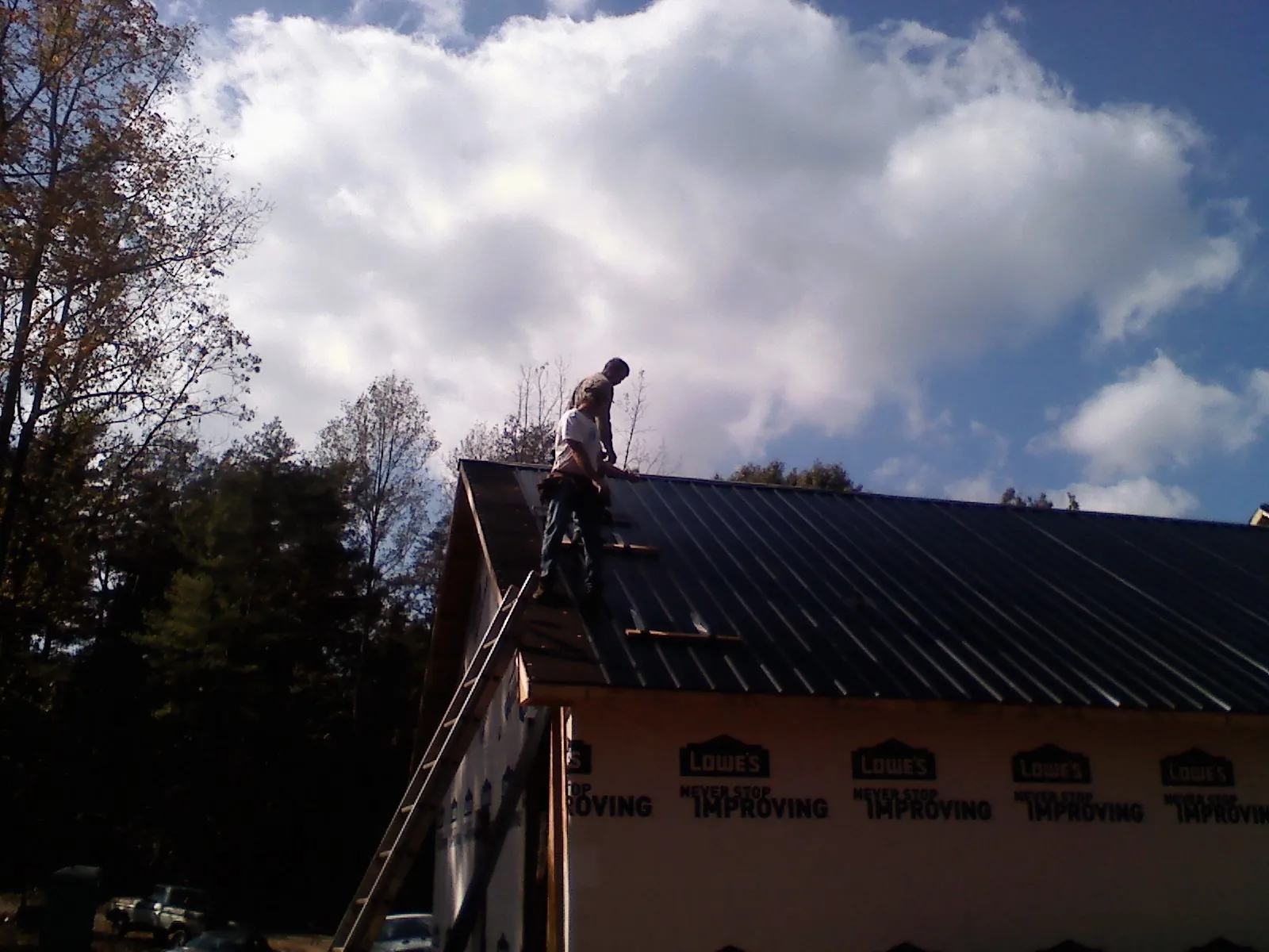 Roofer fastening dark metal panels high against a cloudy sky, from a Roof Inspection job in Gilson