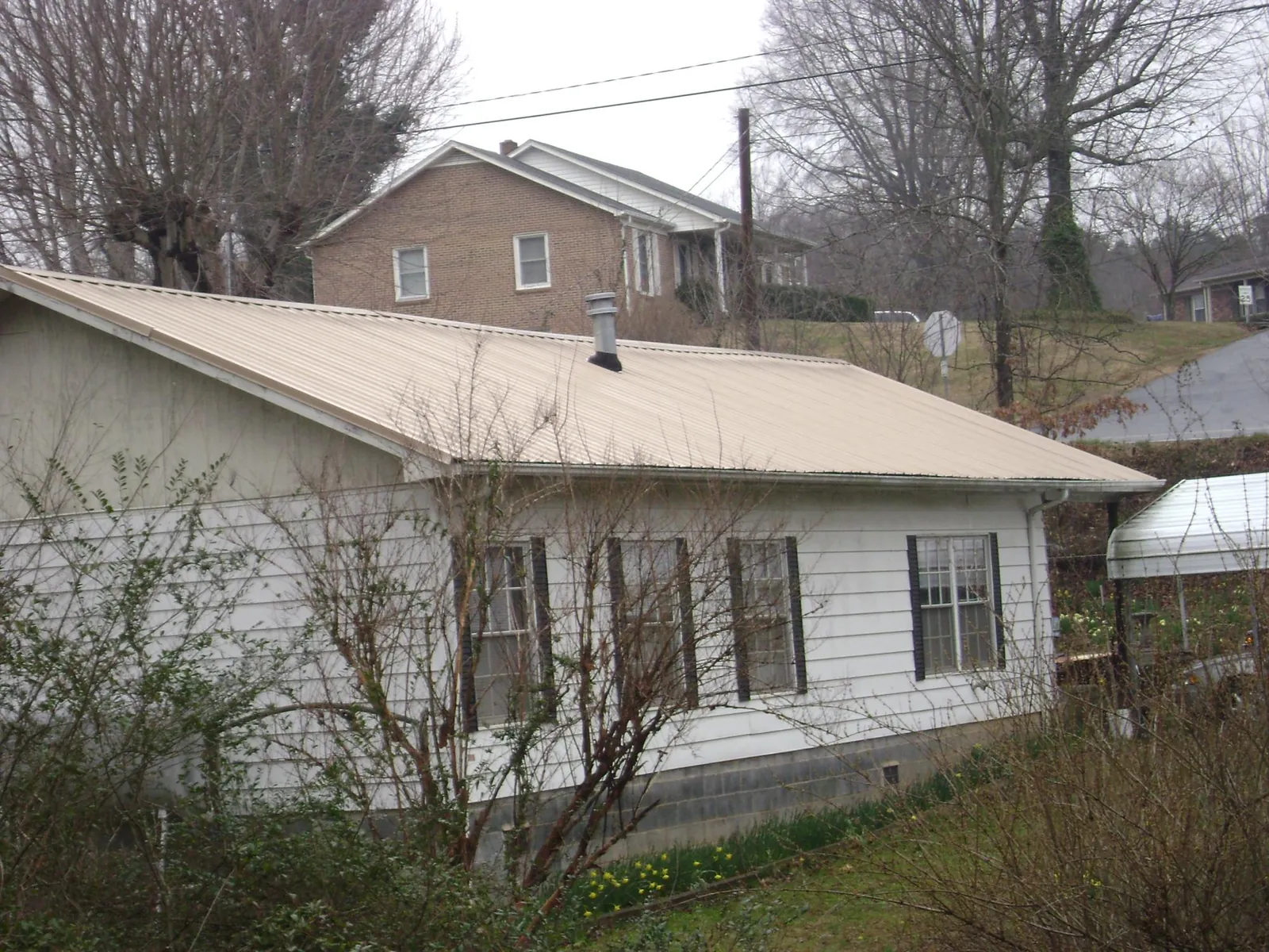 Tan metal roof on a white sided house set into a hillside — Commercial Roofing by Roofing Brothers in Gilson