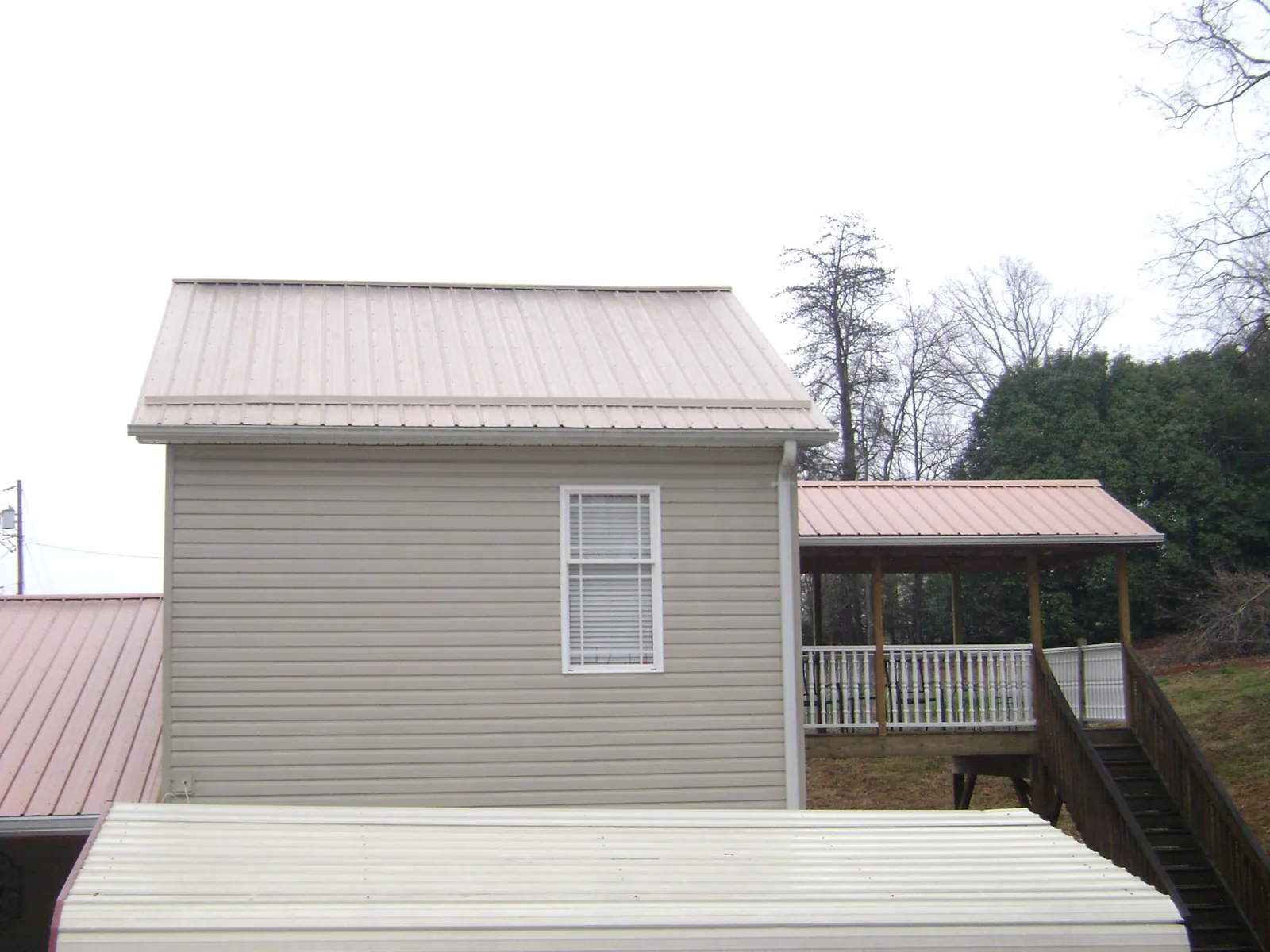 Tan metal roofs on a two story addition and attached porch, from a Roof Replacement job in Gilson